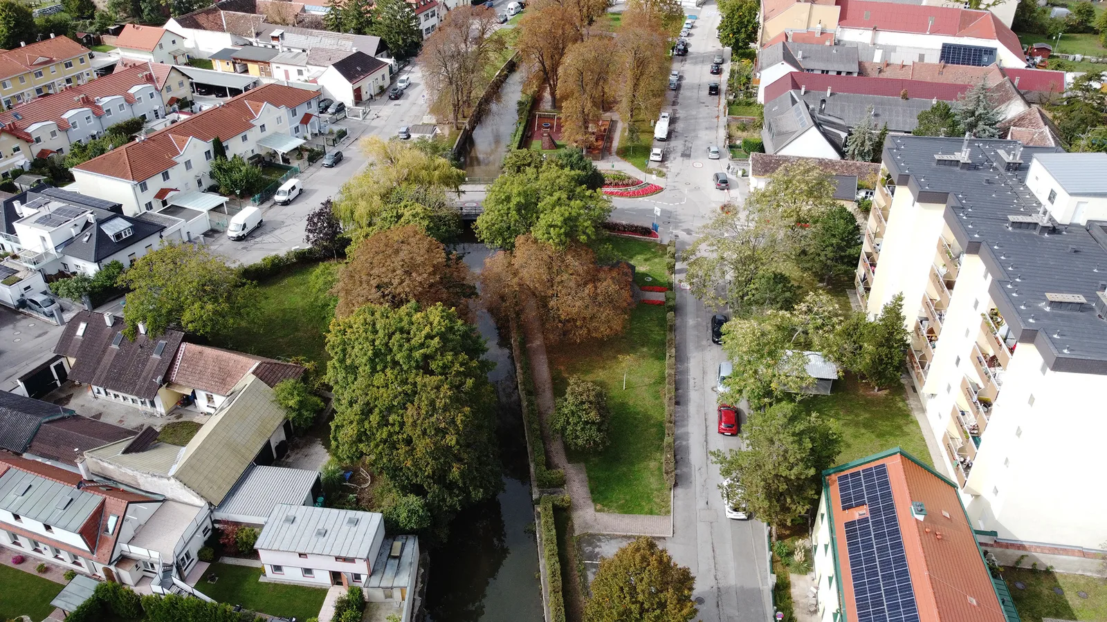 Bestandsaufnahme eines Bachlaufs zwischen Wohnhäusern, Straßen und Grünflächen aus der Luft